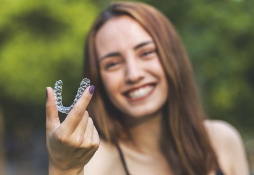 Smiling woman holding Clear Correct aligner and smiling